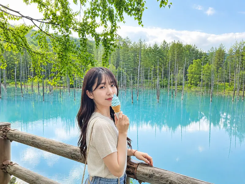 초록 나무와 파란 수면 앞 난간에 선 여행객